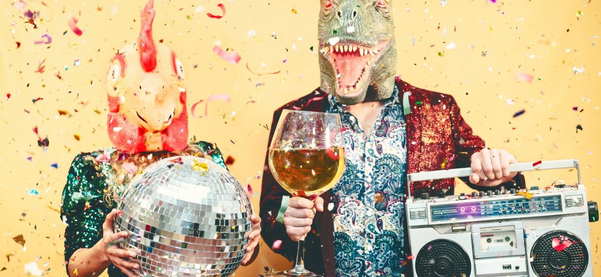 Crazy couple celebrating new year eve wearing chicken and dinosaur t-rex mask - Young trendy people having fun drinking champagne and listening music with vintage boombox - Absurd and holidays concept