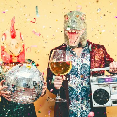 Crazy couple celebrating new year eve wearing chicken and dinosaur t-rex mask - Young trendy people having fun drinking champagne and listening music with vintage boombox - Absurd and holidays concept